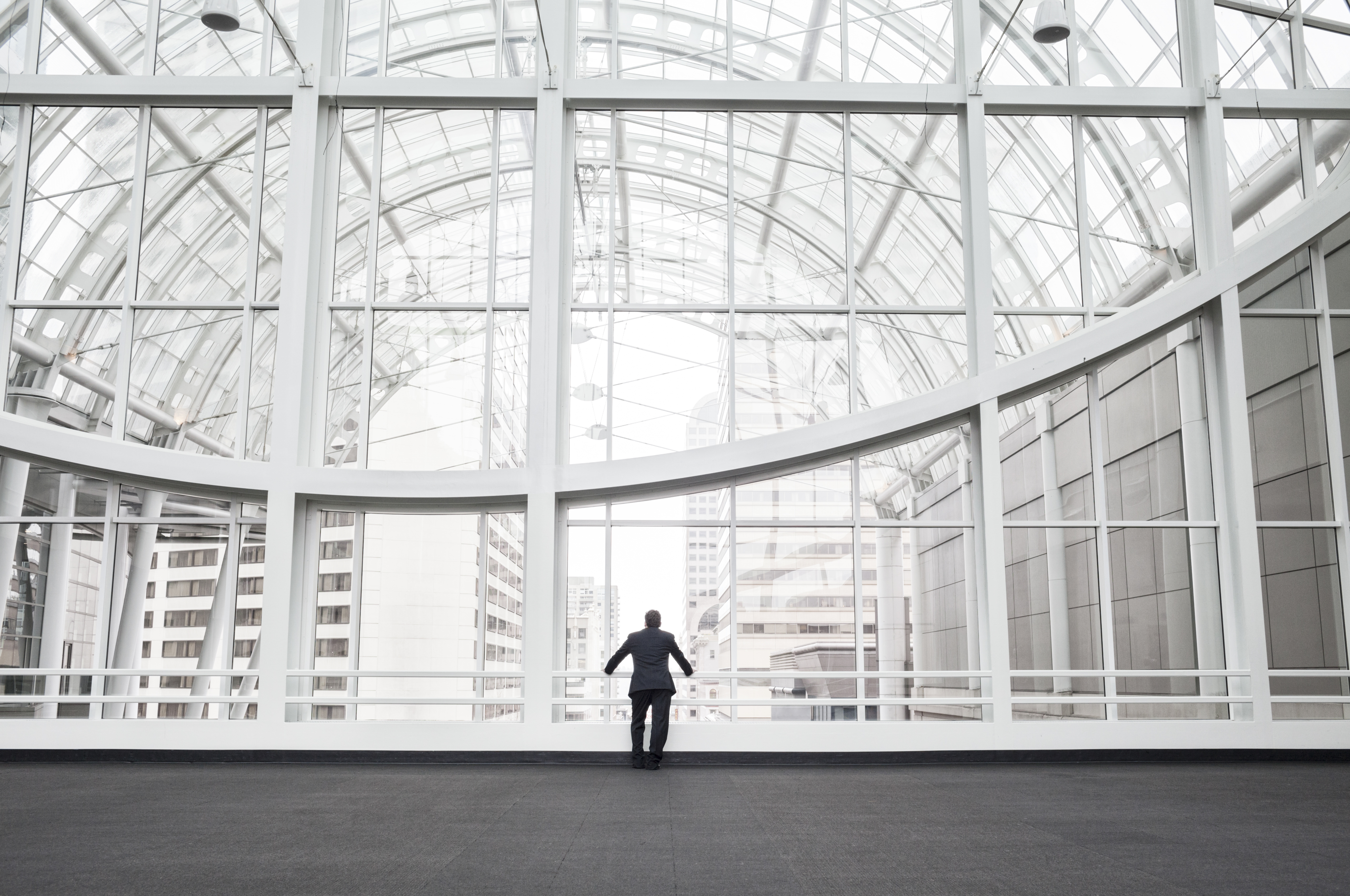 A figure at a glass atrium wall looking out over the city — clarity and perspective on the work ahead.